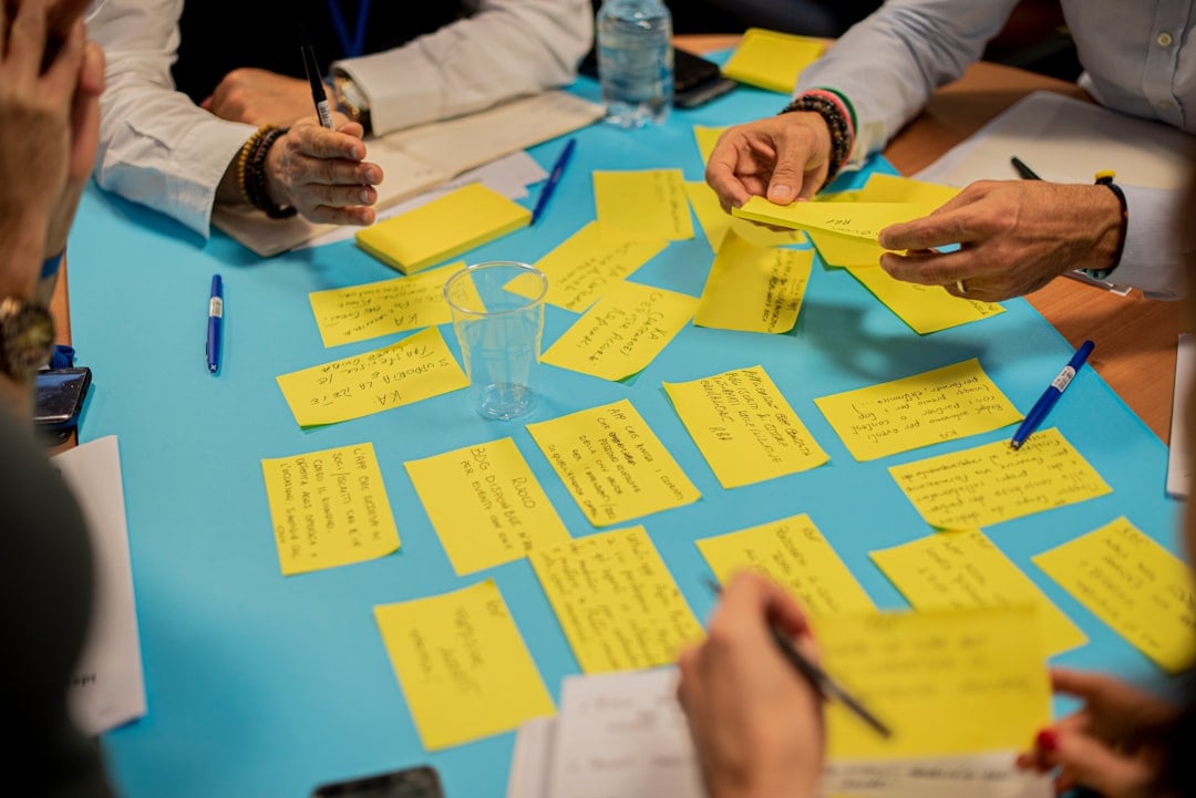 Hände sortieren beschriebene gelbe Haftnotizen auf einem blauen Workshop-Tisch